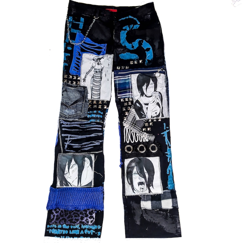 Flat laid black pants with anime prints, colorful patchwork in multiple blue shades, ripped patches, zipper, eyelets, studs and abstract painting with a blue snake on the front.