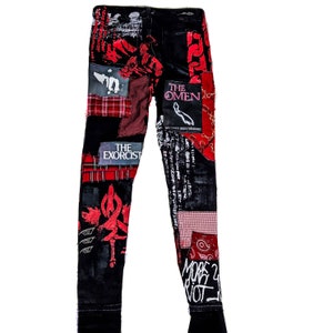 Flat laid skinny custom made black pair with prints containing various horror movies, red and black patchwork, abstract painting, studs, red laces hanging down, chain and eyelets.