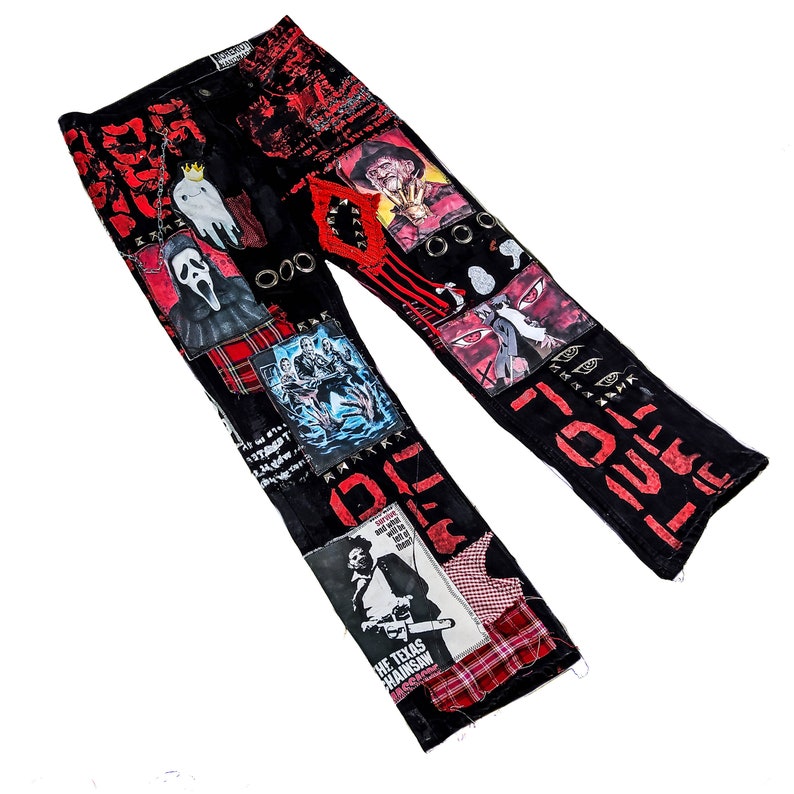 Flad laid jeans showing a custom made black pair with prints containing various horror movies, red and black patchwork, abstract painting, studs, red laces hanging down, chain and eyelets.