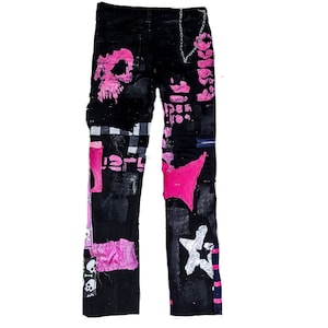 Flat laid pair of pink and black add ons on black pants, such as pink and white skulls, zippers, studs, purple laces and chain, abstract paint and patchwork.