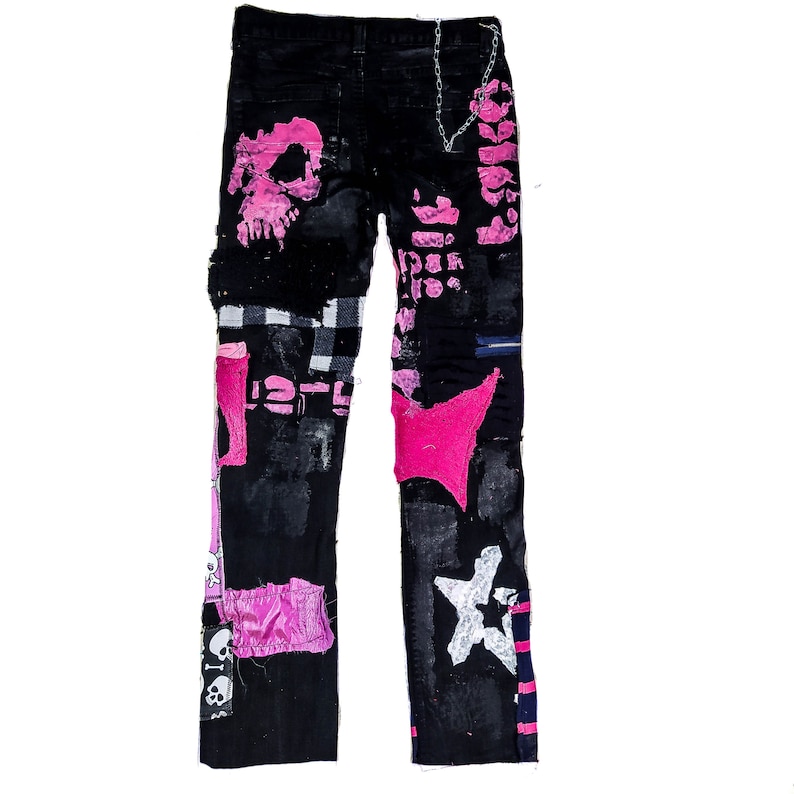 Flat laid pair of pink and black add ons on black pants, such as pink and white skulls, zippers, studs, purple laces and chain, abstract paint and patchwork.