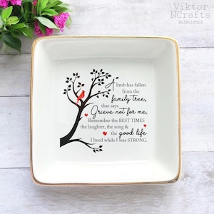 Könnte beinhalten: Eine quadratische, weiße Keramikschale mit goldenem Rand. Die Schale zeigt ein schwarzes Baumdesign mit einem roten Kardinal und dem Text "Ein Ast ist vom Stammbaum gefallen, der sagt Trauert nicht um mich."