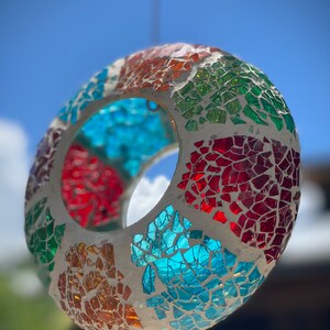 May include: A colorful mosaic glass sphere hanging from a string. The sphere is made of small pieces of glass in shades of red, orange, yellow, green, blue, and white. The sphere has a hole in the center, making it suitable for hanging.