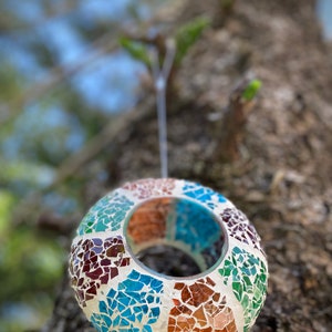 May include: A round, mosaic-tiled, hanging candle holder with a teal, brown, and white color scheme. The holder is made of small, irregular pieces of glass.