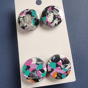 May include: Four round earrings with a black background and colourful abstract patterns. The earrings have a silver, pink, turquoise, and orange colour scheme.