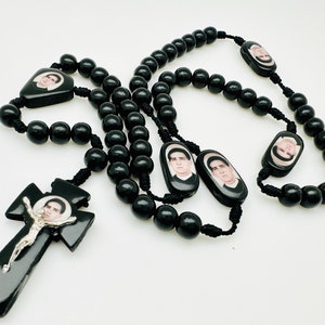May include: Black wooden rosary beads with a black crucifix and five oval-shaped medallions featuring images of a man.