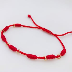 Pulsera roja de 7 nudos adornada con nudos de hilo y unos pequeñitos anillos de oró laminado