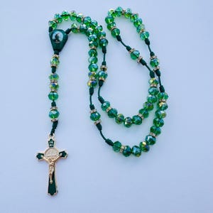 May include: Green crystal rosary beads with a gold-toned crucifix and a green and gold-toned medal. The beads are strung on a green cord.