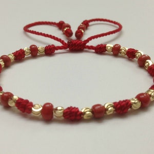 May include: Red and gold bracelet with a knotted cord and small beads.