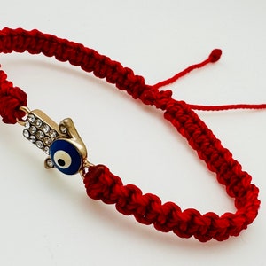 Es una pulsera Roja con mano de Fátima y ojo turco