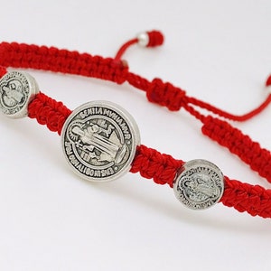 Peut inclure: Bracelet en cordon rouge avec trois médaillons argentés représentant l'image de la Vierge Marie. Les médaillons portent les inscriptions "SEMPER VIRGO MARIA" et "ENS  GRATIAE PLENA" autour des bords.