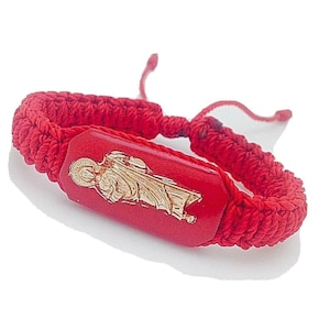 Può includere: Braccialetto intrecciato rosso con una figura religiosa dorata su un ciondolo rettangolare rosso.