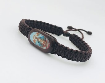 Op de afbeelding: Een bruin gevlochten armband met een ovale houten bedel met een religieus beeld. De bedel heeft een blauw, wit en rood beeld van een vrouw in een blauwe jurk.