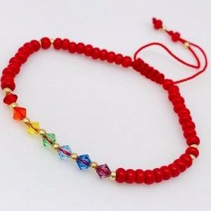 Puede incluir: Pulsera de cuentas rojas con un arcoíris de cuentas de cristal y detalles dorados. La pulsera tiene un cierre de cordón rojo.