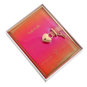 May include: A pink and orange ombre journal with a gold heart-shaped lock and key. The journal is in a white box and has the text "hush-hush" and "VICTORIA'S SECRET" on the cover.