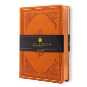 Könnte beinhalten: Ein orangefarbenes Notizbuch mit festem Einband, strukturierter Oberfläche und aufwendigen, geprägten floralen Randmustern. Ein schwarzes horizontales Papierband umschließt die Mitte mit dem goldenen Text Victoria's Journals und dem Zitat Writing is closer to thinking than speaking.