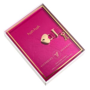 May include: A hot pink journal with a heart-shaped lock and key, presented in a clear box. The journal cover features the words "hush-hush" and "VICTORIA'S JOURNALS". The journal is a beautiful way to take notes.