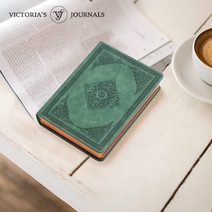 May include: A rectangular journal with a sage green cover featuring an embossed floral pattern and a central decorative motif. The edges of the pages are metallic copper, and the cover displays the text Victoria's Journals at the top.