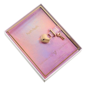 May include: A pink and purple iridescent journal with a heart-shaped lock and key. The journal is in a white box with gold trim. The words "hush-hush" and "VICTORIA'S JOURNALS" are printed on the cover.