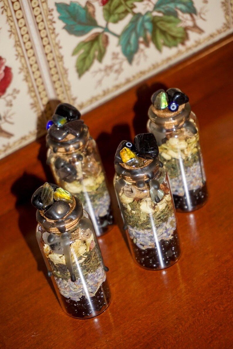 May include: Four small glass bottles filled with dried herbs, flowers, and crystals. The bottles have black wax seals and are topped with various colored crystals.