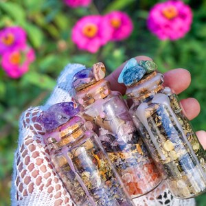 May include: Three small glass bottles filled with dried herbs and crystals. The bottles are topped with cork stoppers and sealed with wax. The bottles are held in a hand wearing a white lace glove.