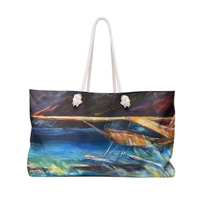 Könnte beinhalten: Große Tragetasche mit einem abstrakten Gemälde in Blau-, Orange- und Gelbtönen. Sie hat weiße Seilgriffe und dekorative weiße Knoten. Das Kunstwerk zeigt eine Meereslandschaft mit dunklem Himmel.