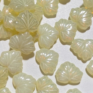 May include: A collection of iridescent white leaf-shaped beads. The beads are made of glass and have a slightly translucent appearance.
