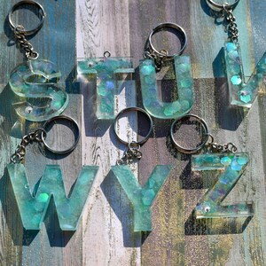 Pu&ograve; includere: Portachiavi con le lettere S, T, U, V, W, Y e Z. Ogni lettera &egrave; realizzata in resina trasparente con una tonalit&agrave; verde acqua e glitter incorporati. I portachiavi hanno anelli e catene in metallo color argento.