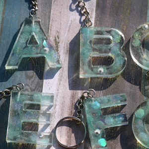 Pu&ograve; includere: Portachiavi con le lettere A, B, C, E, F e G. Ogni lettera &egrave; realizzata in resina trasparente con una tonalit&agrave; verde acqua, incorporata con glitter iridescenti e piccoli elementi decorativi. I portachiavi hanno catene e anelli argentati.