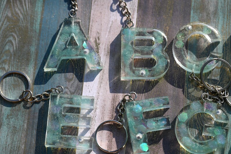 Pu&ograve; includere: Portachiavi con le lettere A, B, C, E, F e G. Ogni lettera &egrave; realizzata in resina trasparente con una tonalit&agrave; verde acqua, incorporata con glitter iridescenti e piccoli elementi decorativi. I portachiavi hanno catene e anelli argentati.