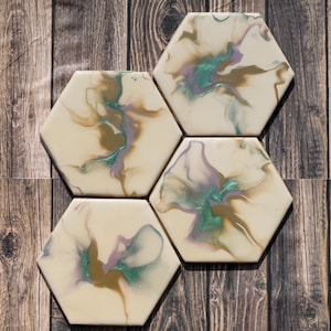 Può includere: Set di sei sottobicchieri esagonali con sfondo bianco e marmiatura astratta in tonalità oro, verde e viola.