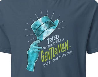 May include: A blue t-shirt with a graphic featuring a teal hat and hand, with the text "TRIED TO DRINK Like A GENTLEMAN... (KEEP YOUR HATS ON)". The shirt has a crew neck and short sleeves.