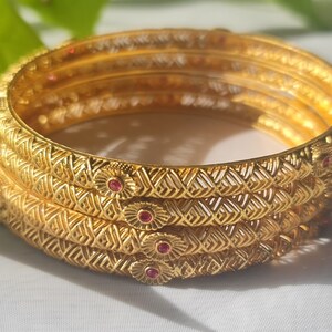 May include: Set of four gold bangles with intricate designs and pink gemstones.