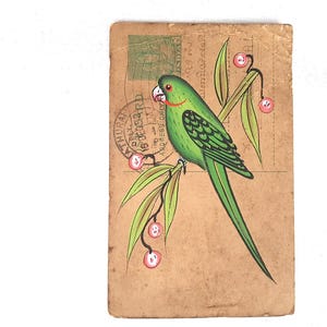 May include: A vintage postcard with a hand-painted green parrot on a branch with red berries. The parrot has a red beak and eye ring. The background is tan with a green stamp and text.