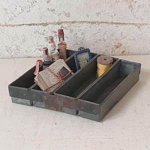 Peut inclure: Un plateau en métal vintage à quatre compartiments, rempli de petites bouteilles, un livre, un cadre photo et une bobine de fil jaune.