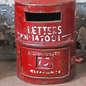 May include: A red metal mailbox with a white painted inscription that reads "LETTERS P.N.-147001" and a white number "75" on the front.