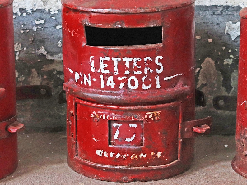 May include: A red metal mailbox with a white painted inscription that reads "LETTERS P.N.-147001" and a white number "75" on the front.