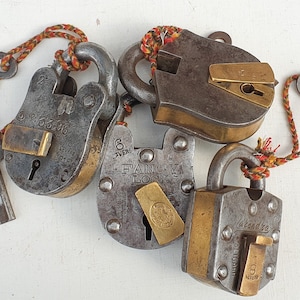 Könnte beinhalten: Vier antike Messing-Schlösser mit aufwendigen Details und gravierten Beschriftungen. Die Schlösser haben unterschiedliche Designs und Größen, darunter ein Schloss mit der Aufschrift "Fancy Lock".