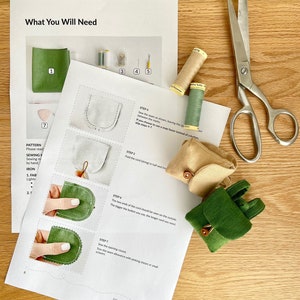 May include: A sewing pattern and instructions for making a small green fabric backpack with a brown button closure. The pattern includes a list of materials needed, such as fabric, thread, and buttons. The instructions are illustrated with step-by-step photos.