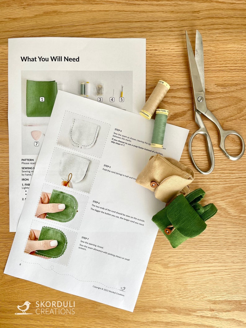 May include: A sewing pattern and instructions for making a small green fabric backpack with a brown button closure. The pattern includes a list of materials needed, such as fabric, thread, and buttons. The instructions are illustrated with step-by-step photos.
