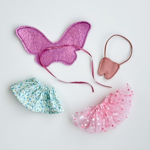 K&ouml;nnte beinhalten: Ein Set aus drei Feen-Kost&uuml;mzubeh&ouml;r: ein rosa Schmetterlingsfl&uuml;gel, ein rosa T&uuml;ll-Tutu mit wei&szlig;en Punkten und ein rosa Filzzahn mit einem braunen Band.