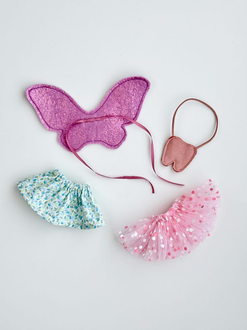 K&ouml;nnte beinhalten: Ein Set aus drei Feen-Kost&uuml;mzubeh&ouml;r: ein rosa Schmetterlingsfl&uuml;gel, ein rosa T&uuml;ll-Tutu mit wei&szlig;en Punkten und ein rosa Filzzahn mit einem braunen Band.