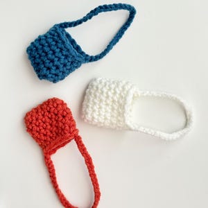 May include: Three handmade crochet bottle holders in blue, white, and red. Each holder has a small pouch with a loop handle. The items are displayed on a white background. The crochet work appears to be tightly knit.