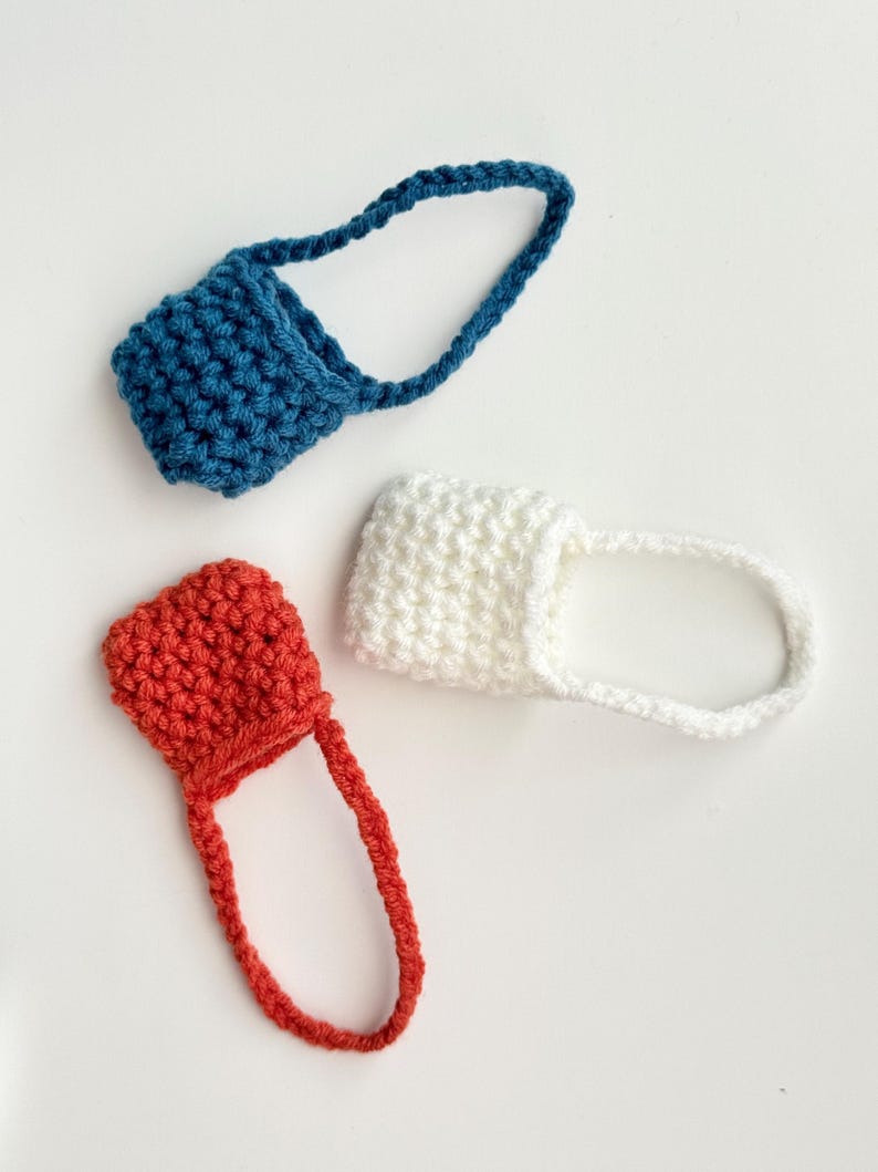 May include: Three handmade crochet bottle holders in blue, white, and red. Each holder has a small pouch with a loop handle. The items are displayed on a white background. The crochet work appears to be tightly knit.