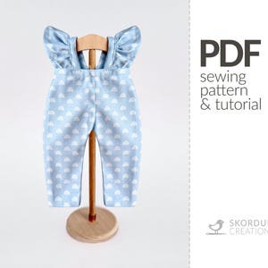 May include: Light blue baby overalls with a white rainbow pattern, displayed on a wooden stand. The overalls have ruffled sleeves and suspenders. Text on the right side reads "PDF sewing pattern & tutorial."