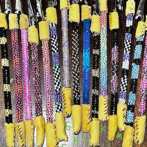 May include: A set of 18 beaded, multi-colored, and patterned clip-on hair ties with leather accents. The hair ties are labeled with letters A through O.