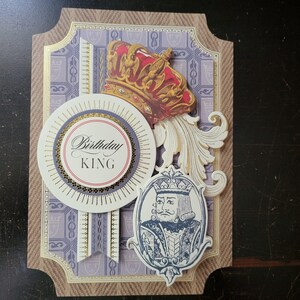 May include: A decorative birthday card with a regal theme. The card features a red and gold crown, a circular emblem with "Birthday KING" text, and an illustration of a king. The background has a patterned design in shades of purple and gold.