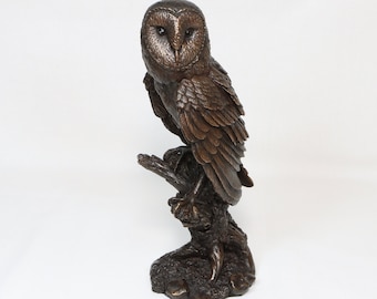 May include: A bronze sculpture of a barn owl perched on a branch. The owl is facing forward with its wings spread out. The sculpture is detailed and realistic.