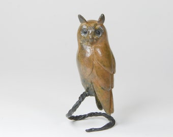May include: A brown and green owl sculpture with black eyes, perched on a black metal branch.