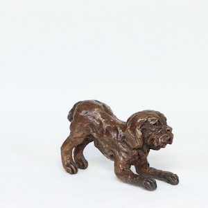 May include: A bronze-colored dog sculpture in a playful pose, with its front legs extended and rear raised. The dog's fur is textured, and the sculpture is set against a white background. This decorative piece is ideal for dog lovers.